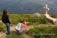 Uns turistes fotografien un cruceiro ubicat a la part posterior del Faro de Fisterra.