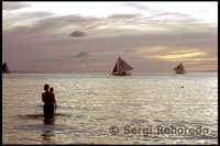 Una pareja se baña al atardecer en un paisaje más que romántico. Bangkas navegando. Atardecer en White beach. Boracay.