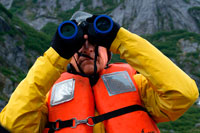 Juneau, Alaska, USA. Passenger with binoculars on cruise ship Safari Endeavour at anchor at Fords Terror, Endicott Arm, Tongass National Forest, Juneau, Alaska, USA. Cliff-walled fjords sliced into the mountainous mainland are on tap today as you slowly slip into an area widely acclaimed as the most beautiful in Alaska.