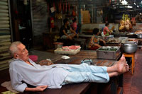 Bangkok. Elder lying and sleeping on a tatami in a Market stall and street food being prepared in Chinatown Bangkok, Thailand. Yaowarat, Bangkok’s Chinatown, is the World’s most renowned street food destination and the local favorite dining district. On this early night adventure, we bring to you discover the sophisticated flavors of Bangkok’s 200 years old community that is rich with Thai-Chinese tradition & delicious food. During the tour you will walk to explore & taste local cuisines from 7 famous eateries, varied from street food vendors to renowned Thai-Chinese diners.