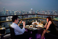 Bangkok. Romantic dinner. Banyan Tree Rooftop Vertigo & Moon Bar, Restaurant, , Bangkok , Thailand. View of the city, Vertigo Bar and Restaurant, roof of the Banyan Tree Hotel, at dusk Bangkok, Thailand, Asia. Reaching for the clouds at Vertigo and Moon Bar on the 61st floor of the Banyan Tree hotel is one of the best ways to end a long day in Bangkok. There is no lack of rooftop bars in town but Vertigo has always been amongst the favourites. With an unusual narrow and elongated shape, the entire top of the building is occupied by both the bar and the restaurant and gives the unusual impression of being aboard a spaceship in the sky. Located on Sathorn road, a very large busy avenue peppered with tall glass and metal skyscrapers and not far from the Lumpini park and Silom area, Banyan Tree is a name often associated with luxury.
