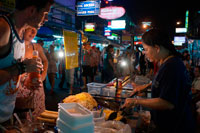 Bangkok. khao san road, noodles street stall. Food stall. Bangkok. Khaosan Road or Khao San Road is a short street in central Bangkok, Thailand. It is in the Banglamphu area of (Phra Nakhon district) about 1 kilometre (0.62 mi) north of the Grand Palace and Wat Phra Kaew. "Khaosan" translates as "milled rice", a reminder that in former times the street was a major Bangkok rice market. In the last 20 years, however, Khaosan Road has developed into a world famous "backpacker ghetto". It offers cheap accommodation, ranging from "mattress in a box" style hotels to reasonably priced 3-star hotels. In an essay on the backpacker culture of Khaosan Road, Susan Orlean called it "the place to disappear". 