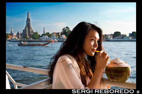Buena chica romántica en un barco cerca de Templo Wat Arun y del río Chao Praya. Beber una coconout. Chao Phraya barco turístico. El BTS Skytrain se da la mano con el proveedor de Bangkok mayor público de agua de transporte, el Chao Phraya Barco expreso Co., Ltd. (Establecido hace 38 años) para introducir un nuevo servicio de transporte de agua "El Chao Phraya barco turístico". Este servicio ofrece a los turistas la oportunidad de ver Bangkok desde una perspectiva totalmente nueva, en un solo día, el turista puede viajar fácilmente en los barcos de alta cantidad de muelle a muelle sin preocuparse por la compra de billetes de barco o perderse. Además, pueden visitar muchos lugares turísticos atractivos tales como el templo del amanecer, y el gran Buda reclinado en Wat Pho. Viaje a lo largo del río Chao Phraya. El río Chao Phraya juega muchos papeles en la vida tailandesa, de hecho, es considerada como la arteria principal de la nación. Gran parte de la historia tailandesa se puede rastrear a lo largo de las bandas del río Chao Phraya. A medida que fluye, el río lleva consigo la historia y la cultura del país. El servicio Chao Phraya Barco Turístico te lleva a 8 muelles diferentes que dan acceso a las atracciones más famosas de Bangkok muchas de las cuales están en el Casco Histórico Rattanakosin Island, que se instaló durante las eras Thonburi y Rattanakosin. Antiguos templos, palacios y comunidades a lo largo de las orillas del río Chao Phraya, nos dicen que el río Chao Phraya ha proporcionado sustento de la gente y ha dado lugar al nacimiento de una civilización.