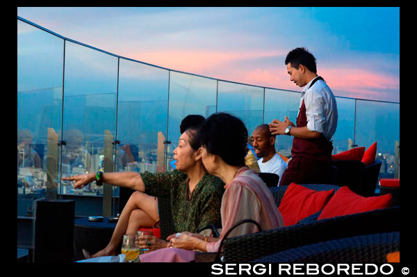 Red Sky Bar Rooftop. Bangkok. Thailand. On the top floor of the Centara Grand skyscraper in the city centre. The view  Chinatown, plus the Grand Palace and temples of Rattanakosin Island. Red Sky is one of the newest rooftop bars and restaurant in Bangkok. While it doesn't offer striking riverside or treetop views that other rooftop bars enjoy, it has pretty impressive 360-degree panoramic vistas from its 55th floor, one of the most convenient locations in town. If you visit Bangkok, chances are you will end up shopping in the Siam area, where the largest and most trendy shopping malls are located, such as the legendary Siam Paragon, MBK and the newly rebuilt CentralWorld. Red Sky bar is part of the Centara Grand Hotel, which itself is actually part of this gigantic CentralWorld shopping mall. So it seems to be a perfect combination: shop till your credit card drops, then recover from walking miles and miles with a dinner or a glass of chilled wine with unforgettable views from the rooftop above the shopping mall itself.