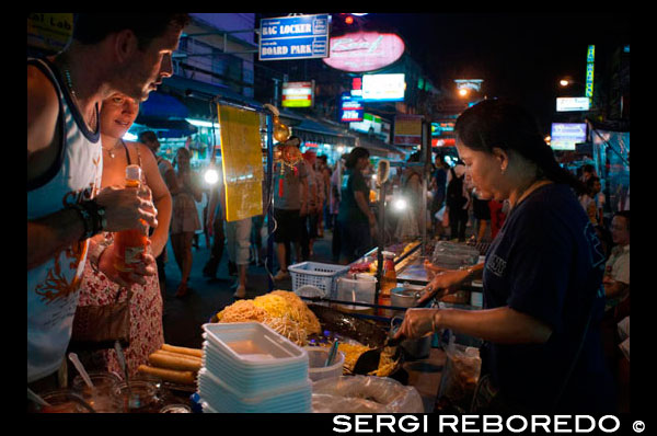Khao San Road, lloc de fideus carrer. Lloc de menjar. Bangkok. Khaosan Road o Khao San Road és un carrer curt al centre de Bangkok, Tailàndia. És a la zona de Banglamphu (districte de Phra Nakhon) prop d'1 quilòmetre (0,62 milles) al nord del Gran Palau i el Wat Phra Kaew. "Khaosan" es tradueix com "arròs blanc", un recordatori que en altres temps el carrer era un important mercat d'arròs Bangkok. En els últims 20 anys, però, Khaosan Road s'ha convertit en un famós "gueto motxiller". Ofereix allotjament econòmic, que van des d'hotels d'estil "matalàs en una caixa" a un preu raonable hotels de 3 estrelles. En un assaig sobre la cultura motxiller de Khaosan Road, Susan Orlean el va anomenar "el lloc de desaparèixer". També és una base del viatge: entrenadors surten tots els dies pels principals destinacions turístiques de Tailàndia, de Chiang Mai, al nord de Ko Pha Ngan, al sud, i hi ha moltes agències de viatges relativament barats que pot organitzar els visats? ? i transport als veïns països de Cambodja, Laos, Malàisia i Vietnam. Botigues Khaosan venen artesanies, pintures, roba, fruites locals, CD pirates, DVDs, una àmplia gamma de documents d'identitat falsos, llibres de segona mà, a més de molts articles motxillers útils. Durant l'última tarda, els carrers es converteixen en bars i es reprodueix la música, els venedors ambulants d'aliments venen insectes a la graella, aperitius exòtics per als turistes, i també hi ha gent flagel·lació espectacles de taula. Hi ha diversos pubs i bars on els motxillers es reuneixen per discutir els seus viatges. La zona és coneguda internacionalment com un centre de ball, la festa, i just abans de l'Any Nou tailandès tradicional (el festival de Songkran) 13-15 d'abril de esquitxades d'aigua que en general es converteix en una enorme guerra d'aigua. Un escriptor tailandès ha descrit Khaosan com "... un camí curt que té el son més llarg del món". [2] Un temple budista sota patrocini reial, la centenària Wat Chana Songkram, és davant de Khaosan Road cap a l'oest, mentre que l'àrea al nord-oest conté una comunitat islàmica i diverses mesquites petites.