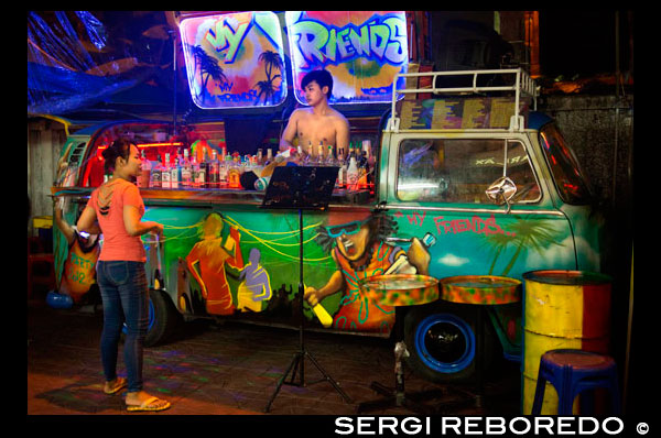 A VW Volkswagen bus cocktail bar in Soi Rambuttri. Bangkok. Grab a beer with ice or a cocktail from one of the pop-up bars and pull up a seat with the locals. The best place to try is along the back of the temple where you can hear some great live music and a friendly and cheerful atmosphere. These places don’t tend to get busy until after 23:00 though. You can also find a couple of the amazing decorated car bars on Rambuttri – a VW campervan and a songtaew. VW bars are converted vans with staff operating the cocktail shakers from inside the Volkswagen. Decorated with neon fairy lights, disco balls and impressive sound systems blaring out the latest pop hits, they’re a noticeable addition to Bangkok party street Sukhumvit 11. Bangkok is a city where you can just as easily find high-end drinking and dining as you can dirt-cheap, down-and-out booze and nosh, and Sukhumvit Soi 11 is one of those rare sois that showcases clubs and bars to suit every budget. The general rule is that the further you venture up the soi, the more expensive the options get. However, the VW bars, dotted along the entire street, are about as cheap as it gets, and allow you to become lubricated under the gaze of the notoriously expensive Bed Supper Club, without putting so much as a chink in your wallet.