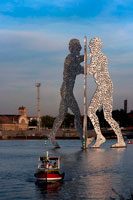 Berlin. Germany. Metallic sculpture called Molecule Man by Jonathan Borofsky in Spree River Berlin. Molecule Man is a series of aluminium sculptures, designed by American artist Jonathan Borofsky, installed at various locations in the world, including Berlin, Germany, and Council Bluffs, Iowa, USA. The first Molecule Man sculptures were made in 1977 and 1978 in Los Angeles, USA. The sculptures consist of three humans leaning towards each other, the bodies of which are filled with hundreds of holes, the holes representative of "the molecules of all human beings coming together to create our existence". A related sculpture is the Hammering Man
