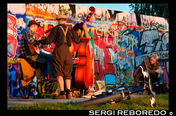Musicians. Buskers by the Wall in Mauerpark Berlin in evening light Germany. Mauerpark is a public linear park in Berlin's Prenzlauer Berg district. The name translates to "Wall Park", referring to its status as a former part of the Berlin Wall and its Death Strip. The park is located at the border of Prenzlauer Berg and Gesundbrunnen district of former West Berlin. In the 19th and 20th centuries, the Mauerpark area served as the location of the Old Nordbahnhof ("Northern Railway Station"), the southern terminus of the Prussian Northern Railway opened in 1877-78, which connected Berlin with the city of Stralsund and the Baltic Sea. Soon after it lost its role as a passenger station to the nearby Stettiner Bahnhof and remained in use as a freight yard. In 1950 the Stettiner Bahnhof took the name Nordbahnhof because of its role in Berlin's public transportation system, and the Old Nordbahnhof became known as Güterbahnhof Eberswalder Straße. It was finally closed after the building of the Berlin Wall in 1961. When viewed from above, one can still see remains of the railroad tracks running towards the former station from the Ringbahn.