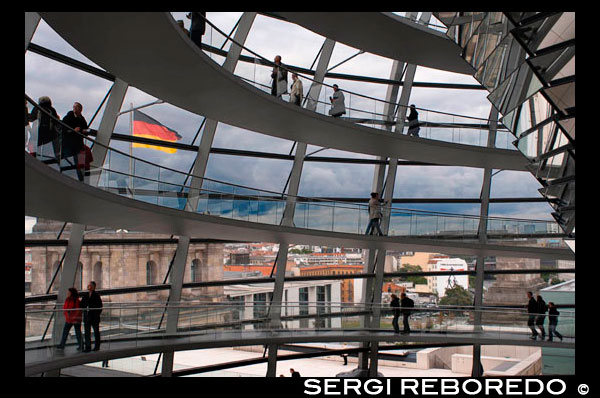 Mirall de con a l'interior del Dom de Reichstag , al parlament alemany ( Reichstag ) , Berlín . L'actual cúpula del Reichstag és una cúpula de vidre emblemàtic construït a la part superior de l'edifici reconstruït de Reichstag a Berlín . Va ser dissenyat per l'arquitecte Norman Foster i construït per simbolitzar la reunificació d'Alemanya. L'aspecte distintiu de la cúpula s'ha convertit en un emblema de la ciutat de Berlín . La cúpula del Reichstag és una gran cúpula de vidre amb una vista de 360 graus del paisatge urbà de Berlín circumdant . La càmera de debats del Bundestag , el Parlament alemany , es pot veure més avall . Un con de mirall al centre de la cúpula dirigeix ??la llum del sol a l'edifici . La cúpula està oberta al públic i es pot arribar pujant dos acer en espiral de rampes que són una reminiscència d'una doble hèlix . La cúpula de vidre també va ser dissenyat per Foster per ser amigable amb el medi ambient . Característiques d'eficiència energètica que impliquin l'ús de la llum del dia que brilla a través del con de mirall es van aplicar , reduint eficaçment les emissions de carboni de l'edifici . El disseny futurista de la cúpula del Reichstag fa que sigui un punt de referència únic , i simbolitza l'intent de Berlín a allunyar d'un passat del nazisme i el comunisme i en lloc de cap a un futur amb un major èmfasi en una Sud-àfrica unida , Alemanya democràtica