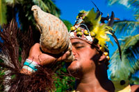 Aitutaki. Cook Island. Polynesia. South Pacific Ocean. An actor dressed Polynesian blowing a conch shell in Aitutaki Punarei Culture Tours. This is a unique opportunity for you to learn about the ancient culture, myths, legends and traditional ways of our ancestors. The tour is a great way to discover the history, traditional skills, Art & beliefs of the island of Aitutaki. The tour concludes with a traditional feast (umu kai) for lunch on site. The second voyagers of note were Te Erui and his brother Matareka. Te Erui set out from Havaiki in the canoe Viripo, An unexpected hurricane, hur1'hia, dismasted his vessel, but he managed to get back to Havaiki. On being told by a priest that the cause of the disaster was due to the naming of his canoe, he immediately built another canoe. The vessel, on the advice of the priest, was named Te Rangi-pae-uta, and the two masts were named after the gods Rongo and Tangaroa. Thus, with divinity sitting in the belly of his sail, he braved the sea once more in his quest of land. He landed on the West side of Aitutaki, at a point on the reef known as Te Rua-karae. Here he was opposed by one of Ru's descendants, who said, "Tera te moana uriuri o Hiro. Haere ki i'eira kimi henua ai " – "There lies the purple sea of Hiro. Go there to.seek land." The request went unheeded. After slaying various opponents, Te Erui cut a channel through the reef with his adze, Haumapu, and finally settled down at Reureu. The channel which is credited to Te Erui's engineering ability is Te Rua-i-kakau, the boat passage which has been such an inestimable boon to Aitutaki. The various historical spots mentioned are shown on the map of Aitutaki. Ruatapu, the third voyager of note, came from Taputapuatea to Rarotonga, and then successively to Raro-ki-tonga, Mauke, and Atiu. During these voyages his canoe had the name of Te Kareroa-i-tai. At Atiu, the canoe name was changed to Tuehu-moana, and in it he sailed to Manuae and then Aitutaki. 