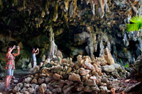 Atiu Island. Cook Island. Polynesia. South Pacific Ocean. Several tourists photographing the impressive Kopeka Bird Caves in Atiu.  These caves are the home to the Kopeka Birds, unique to Atiu. This swift like bird nests deep within the caverns and navigates in the dark by using an echo locating series of clicks. Hear the legend of Inutoto and Tangaroa and learn of the flora and fauna found in the makatea (raised coral) surroundings. Bring your swimwear and enjoy a candle-lit swim in the artesian water pool.  Nurau and Vai Akaruru water caves are fun to swim. Nurau has a vertical sinkhole that drops down from the cave floor to a new level completely underwater. This sinkhole is the entrance to an underwater labyrinth incompletely explored in 1997 by Australians David Goldie and Paul Tobin. Diffuse light filters down to the waters in Vai Akaruru cave making this cave easy to swim. Te Ana O Raka is an easily accessed burial cave. However as Aue Raka's ancestors are interred in this cave it is important to gain permission to enter. Aue offers a tour of the cave and points of interest in the area Ph 33256. Pau Atea cave is long and has many passages. There are many other caves in the area and these are thought to interconnected. It is easy to get lost in these caves. Atiu is a volcanic island surrounded by a coral reef, cliffs and raised coral limestone called makatea. 