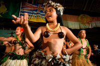 Atiu Island. Cook Island. Polynesia. South Pacific Ocean. Children dressed in traditional Polynesian dances and interpret Polynesian dances organized at Hotel Villas Atiu Atiu island. The Cook Islands lie northeast of New Zealand in the South Pacific Ocean. Cook Islanders are related to the Maori of New Zealand and the inhabitants of French Polynesia (commonly referred to as Tahiti). Cook Islands dance traditions are kept alive through festivals, celebrations and performances for tourists. Cook Islanders living abroad in the United States, Australia and New Zealand perform their dances as a form of cultural preservation.   Dances of the Cook Islands have much in common with other Polynesian dance forms. More widely known dance styles such as the hula from Hawaii and the tamure from Tahiti share similar mythology and dance themes. Cook Island dance performances often include chanting and singing among the dances, which tell stories or serve as spiritual communion with the Polynesian deities. Women’s Choreography: Men and women dance together in performances, though in separate groups. The women’s movements feature side-to-side movements of the hips. These movements are controlled by the knees. The hips must be energetic, with large, pronounced moves, but the upper body must stay graceful, with the shoulders remaining still. Some movement in the arms and hands may accompany the dance, but it must be carefully controlled. Men’s Choreography:  While the women’s silhouette is vertical with movements centered on the hips, men dance closer to the ground, with stronger movements in a distinctive bent-knee pose. 