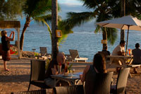 Rarotonga Island. Cook Island. Polynesia. South Pacific Ocean. Tourists photographing the sea and enjoying the sunset on the beach of the Hotel Crown Beach Resort & Spa.  Mixing the best of old and new, the unusually-shaped thatched villas at the Crown Beach combine traditionally inspired architecture with top-drawer decor. The octagonal bungalows are all impeccably finished with blonde-wood panelling, wicker furniture and local artwork on the walls. As with elsewhere on the island, you'll be faced with a choice between paying a premium for a beachfront position or cutting costs by choosing a villa set back slightly from the sand. Scattered over 4.5 acres of private gardens, the 22 villas are sensitively placed with plenty of space between each unit, and the private patios are all intelligently angled for maximum privacy and optimum island views. The atmosphere is elegant and refined, and it's also usually substantially quieter than Rarotonga's other better-known resorts, but the service and facilities are every bit as good as you'd expect for a hotel in this price bracket. There are two on-site restaurants (the fine-dining Windjammer and a more informal beachfront bistro-bar), a spa and massage centre, a giftshop, a babysitting service, and you can even get a free introductory dive on Sundays.