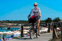 Formentera. Es Pujols, beach, Formentera. Girl riding bicycle. Panoramic view, parasol, deck chair, tourism, holiday. Spain, Balearic Islands, south of Ibiza island, Formentera island, Es Pujols beach.