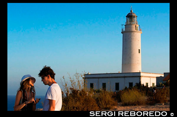 Sunset. Young couple tourists in the Lighthouse, Faro de la Mola, Formentera, Pityuses, Balearic Islands, Spain, Europe. The lighthouses at the port of La Savina, La Mola and Es Cap de Barbaria are located in places of incomparable beauty that deserve a visit thanks to their spectacular scenery.  The lighthouse at La Mola is the oldest and most important. The island's highest lighthouse, it was built on a 120-metre-high cliff,. Enjoying the sunrises and sunsets from this point is an unforgettable, magical experience according to famous writer Jules Verne, who used the lighthouse as the setting for a brief episode in his novel Hector Servadac and who is commemorated by a plaque at the site. 