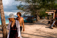 Some tourists walk along a promenade that runs along the side of the east side of the island, where they coalesce most hotels. Gili Meno.