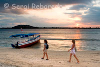 Two women walk along the sandy beach in the west of the island, near the pier Bounty Resort. Gili Meno.