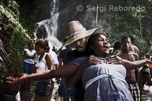 A couple of Haitians by the waterfall of Saut d'eau. Haitian Voodoo officiants are simplicity in dress and attributes that attach to it as a clear religious reference. Not so among his descendants who hold similar hierarchies in those notes, however, an overload in the visible elements. So are multiple types of seed bead necklaces which are made with those sold in some public places. These insert other objects such as plates and key chains called "tears" of crystal chandeliers. In a note collar dozens of spools of sewing threads of different colors. It is clear that the cultural function added decorative elements. Not lacking in these attributes gold medals with pictures of St. Barbara or the Virgin of Caridad del Cobre.