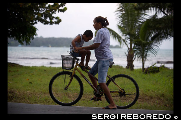 Mother with his kid in a bicycle. Bocas del Toro, Panama. Bocas del Toro (meaning "Mouth of the Bull") is a province of Panama. Its area is 4,643.9 square kilometers, comprising the mainland and nine main islands. The province consists of the Bocas del Toro Archipelago, Bahía Almirante (Almirante Bay), Laguna de Chiriquí (Chiriquí Lagoon), and adjacent mainland. The capital is the city of Bocas del Toro (or Bocas Town) on Isla Colón (Colón Island). Other major cities or towns include Almirante and Changuinola. The province has a population of 125,461 as of 2010.  Christopher Columbus and his crew first visited the area in 1502. Bocas del Toro borders the Caribbean Sea to the north, Limón Province of Costa Rica to the west, Chiriquí Province to the south, and Ngöbe-Buglé Comarca to the east. The Río Sixaola forms part of the border with Costa Rica. An old railroad bridge spans the river between Guabito and Sixaola, Costa Rica. The bridge is a border crossing used by tourists going between destinations in Bocas del Toro and Costa Rica.  The province contains two national parks, Isla Bastimentos National Marine Park and La Amistad International Park. The Smithsonian Tropical Research Institute operates a research station on Colón Island just northwest of Bocas Town. There are many banana plantations in Bocas del Toro, often called the oro verde, or green gold of Central America.