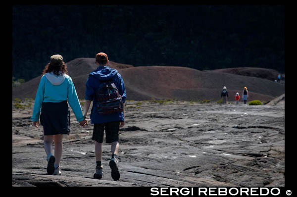 A couple making a trek over the lava of volcano Piton de la Fournaise. Reunion Island is formed by two volcanoes stratum mainly basaltic composition, juxtaposed on the ocean floor and partially emerged: the Piton des Neiges northwest, oldest and extinct 20,000 years ago, culminating at 3070 m. The Piton de la Fournaise is an active volcano that formed on the southeast side of the first and reaches 2631m altitude. The total volume emerged island km3 represents 0.8 x103 to be 1/32 of the total volume of the overall structure. Taking into account the hidden volume in the monoclinal fold of the plate, the part above represents only one hundredth of the total volume. The first eruptive events on the ocean floor at 4000 m depth are estimated occurred 4-5 my ago, the Piton des Neiges has now reached about 7000 m in height from the bottom of the ocean.