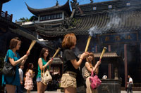 God Temple and pagoda, buddhist temple in Shanghai, burning joss sticks, incense. A women prays and laughs at Chenghuang Miao or City God Temple in Yu Yuan Gardens bazaar Shanghai, China. Located next to the Yuyuan Garden and also known today as the Yu Garden Market, the City God Temple (Chenghuang Temple) was built in the fifteenth century during the Ming Dynasty. Originally a temple built to honor the Han statesman Huo Guang (68 B.C.) The City God Temple is a Taoist temple which is composed of many halls such as the Grand Hall, Middle Hall, Bedroom Palace, Star Gods Hall, Yama Palace, Xuzhen God Hall. The temple had an area of more than 10,000 square meters including two gardens: West Garden (Yuyuan Garden) and East Garden. The City God Temple has a great influence on the residents of Shanghai. The religious festivals of the temple are considered to be the festivals for all Shanghai people.