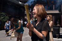 God Temple and pagoda, buddhist temple in Shanghai, burning joss sticks, incense. A women prays and laughs at Chenghuang Miao or City God Temple in Yu Yuan Gardens bazaar Shanghai, China. Located next to the Yuyuan Garden and also known today as the Yu Garden Market, the City God Temple (Chenghuang Temple) was built in the fifteenth century during the Ming Dynasty. Originally a temple built to honor the Han statesman Huo Guang (68 B.C.) The City God Temple is a Taoist temple which is composed of many halls such as the Grand Hall, Middle Hall, Bedroom Palace, Star Gods Hall, Yama Palace, Xuzhen God Hall. The temple had an area of more than 10,000 square meters including two gardens: West Garden (Yuyuan Garden) and East Garden.