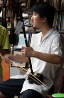 Playing traditional music instrument in Ancient Town of Shanghai. Stringed instrument called Sanxian. The sanxian  is a Chinese lute — a three-stringed fretless plucked musical instrument. It has a long fingerboard, and the body is traditionally made from snake skin stretched over a rounded rectangular resonator. It is made in several sizes for different purposes and in the late 20th century a four-stringed version was also developed. The northern sanxian is generally larger, at about 122 cm in length, while southern versions of the instrument are usually about 95 cm in length. The sanxian has a dry, somewhat percussive tone and loud volume similar to the banjo. 