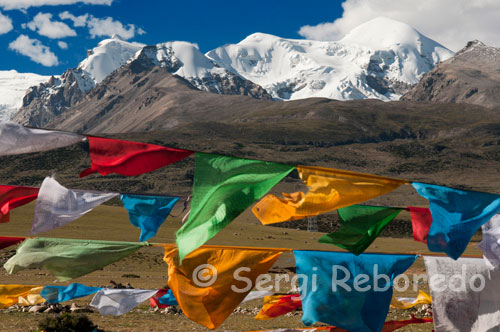 Banderas de oración en la base del Monte Nyenchen Tanglha de 7111 metros de altura. Las banderas tibetanas de oración flamean sobre todo el mundo de la cultura tibetana. Una típica bandera de oración tiene en su imagen central un caballo que porta en su espalda las Tres Joyas en llamas. Este caballo es conocido como el Caballo de Viento y le otorga a las banderas su nombre en tibetano "Lung-Ta". Las tres joyas simbolizan a Budha (el estado de Iluminación), el Dharma (las Enseñanzas budistas) y la Sangha (la Comunidad budista).