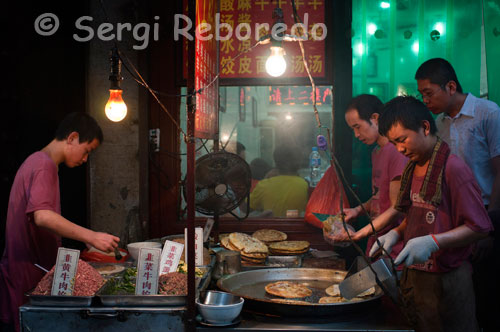 Lloc de menjar de carrer al barri musulmà de Xi'an.; Els estrets carrerons estan plens de carnisseries, fàbriques d'oli de sèsam; petites mesquites amagades després enormes portes de fusta i homes amb poblades barbes i turbants blancs ....