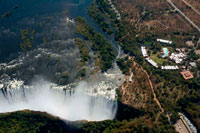 Aerial views of the Victoria Falls. Victoria Falls present a spectacular sight of awe-inspiring beauty and grandeur on the Zambezi River, forming the border between Zambia and Zimbabwe. It was described by the Kololo tribe living in the area in the 1800’s as ‘Mosi-oa-Tunya’ – ‘The Smoke that Thunders’. In more modern terms Victoria Falls is known as the greatest curtain of falling water in the world. Columns of spray can be seen from miles away as, at the height of the rainy season, more than five hundred million cubic meters of water per minute plummet over the edge, over a width of nearly two kilometers, into a gorge over one hundred meters below. The wide, basalt cliff over which the falls thunder, transforms the Zambezi from a placid river into a ferocious torrent cutting through a series of dramatic gorges. 