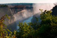 Views of Victoria Falls. Behind, the bridge between Zambia and Zimbabwe.  For more than 50 years the bridge was crossed regularly by passenger trains as part of the principal route between the then Northern Rhodesia, southern Africa and Europe. Freight trains carried mainly copper ore (later, copper ingots) and timber out of Zambia, and coal into the country. The age of the bridge and maintenance problems have led to traffic restrictions at times. Trains cross at less than walking pace and trucks were limited to 30 t, necessitating heavier trucks to make a long diversion via the Kazungula Ferry or Chirundu Bridge. The limit was raised after repairs in 2006, but more fundamental rehabilitation or construction of a new bridge has been aired. During the Rhodesian UDI crisis and Bush War the bridge was frequently closed (and regular passenger services have not resumed successfully). In 1975, the bridge was the site of unsuccessful peace talks when the parties met in a train carriage poised above the gorge for nine and a half hours. In 1980 freight and road services resumed and have continued without interruption except for maintenance. 