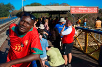 People around Victoria Falls Bridge. The Victoria Falls Bridge crosses the Zambezi River just below the Victoria Falls and is built over the Second Gorge of the falls. As the river is the border between Zimbabwe and Zambia, the bridge links the two countries and has border posts on the approaches to both ends, at the towns of Victoria Falls, Zimbabwe and Livingstone, Zambia. For more than 50 years the bridge was crossed regularly by passenger trains as part of the principal route between the then Northern Rhodesia, southern Africa and Europe. Freight trains carried mainly copper ore (later, copper ingots) and timber out of Zambia, and coal into the country. The age of the bridge and maintenance problems have led to traffic restrictions at times. Trains cross at less than walking pace and trucks were limited to 30 t, necessitating heavier trucks to make a long diversion via the Kazungula Ferry or Chirundu Bridge. 