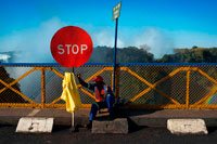 Stop sign at the Zambia and Zimbabwe border bridge. The Victoria Falls Bridge is 100 years old in 2005.  The Victoria Falls Bridge was the brainchild of Cecil Rhodes, a key feature in his dream of a Cape to Cairo railway, even though he never visited the Victoria Falls and died two years before the railway reached them - before construction of the Bridge had begun. The preliminary surveying of the ground for the bridge was made in 1900-01, during the time the Boer War was raging; communications southwards were cut, and the construction of the railway to Victoria Falls was much delayed, but never quite suspended, throughout military operations. The arena of the war did not include Rhodesia, and the work of railway construction never ceased throughout the whole period. In 1900 Rhodes was asked to write a forward for the book 'From Cape to Cairo' by Grogan and Sharp. Ewart Scott Grogan, together with Harry Sharp undertook the epic overland journey from the Cape to Cairo, although Grogan was the only one to complete the entire journey, and thus become the first man to achieve such an undertaking. 