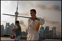 CHINA: Shanghai, morning tai chi exercise on The Bund. Shanghi Bund : Early morning tai chi exercises with swords on the Bund in Shanghai China. The best taichi lessons I've had were from an old guy who practiced outside at 7am every morning. I learned 4 excellent techniques that I still use in my MMA training on a regular basis- a method of catching a kick and throwing your opponent, redirecting a straight punch and countering in the same motion, countering double underhooks with a throw, and escaping a shoulder lock while setting up your own.  It's a really fascinating martial art because every one of those dance like movements represents a simple practical fighting technique or strategy, but it's hard to see how the movements translate into combat applications without a master of the art demonstrating it. But either way even without a kungfu master, the forms themselves are great low impact exercise that you can find everywhere in the city for free every morning.   Most of the old folks in the parks won't mind if you tag along, just show up early and make sure to ask first if it's okay to join them.  The Bund (which means the "Embankment") refers to Shanghai's famous waterfront running along the west shore of the Huangpu River, forming the eastern boundary of old downtown Shanghai. Once a muddy towpath for boats along the river, the Bund was where the foreign powers that entered Shanghai after the Opium War of 1842 erected their distinct Western-style banks and trading houses. From here, Shanghai grew into Asia's leading city in the 1920s and 1930s, a cosmopolitan and thriving commercial and financial center. Many of the awesome colonial structures you see today date from that prosperous time and have become an indelible part of Shanghai's cityscape. After 1949, the street came to symbolize Western dominance over China and was shuttered. 