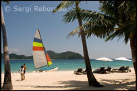 Tourists take in the sun under umbrellas. Sailing boat for the island of Pangulasian. Palawan.